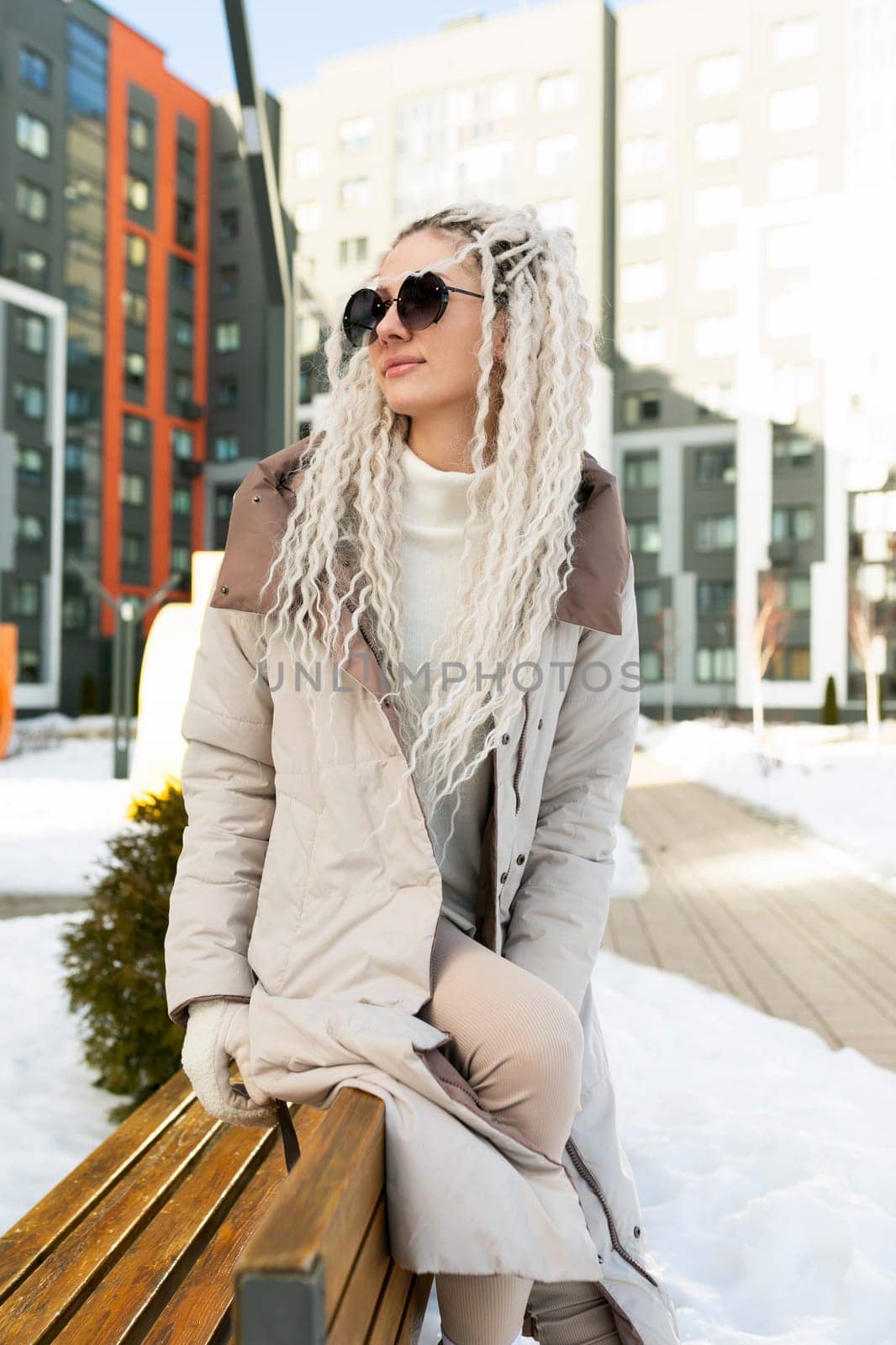 A woman is seated on the top of a sturdy wooden bench, with her feet firmly planted on the ground. She appears relaxed and contemplative, taking in her surroundings.