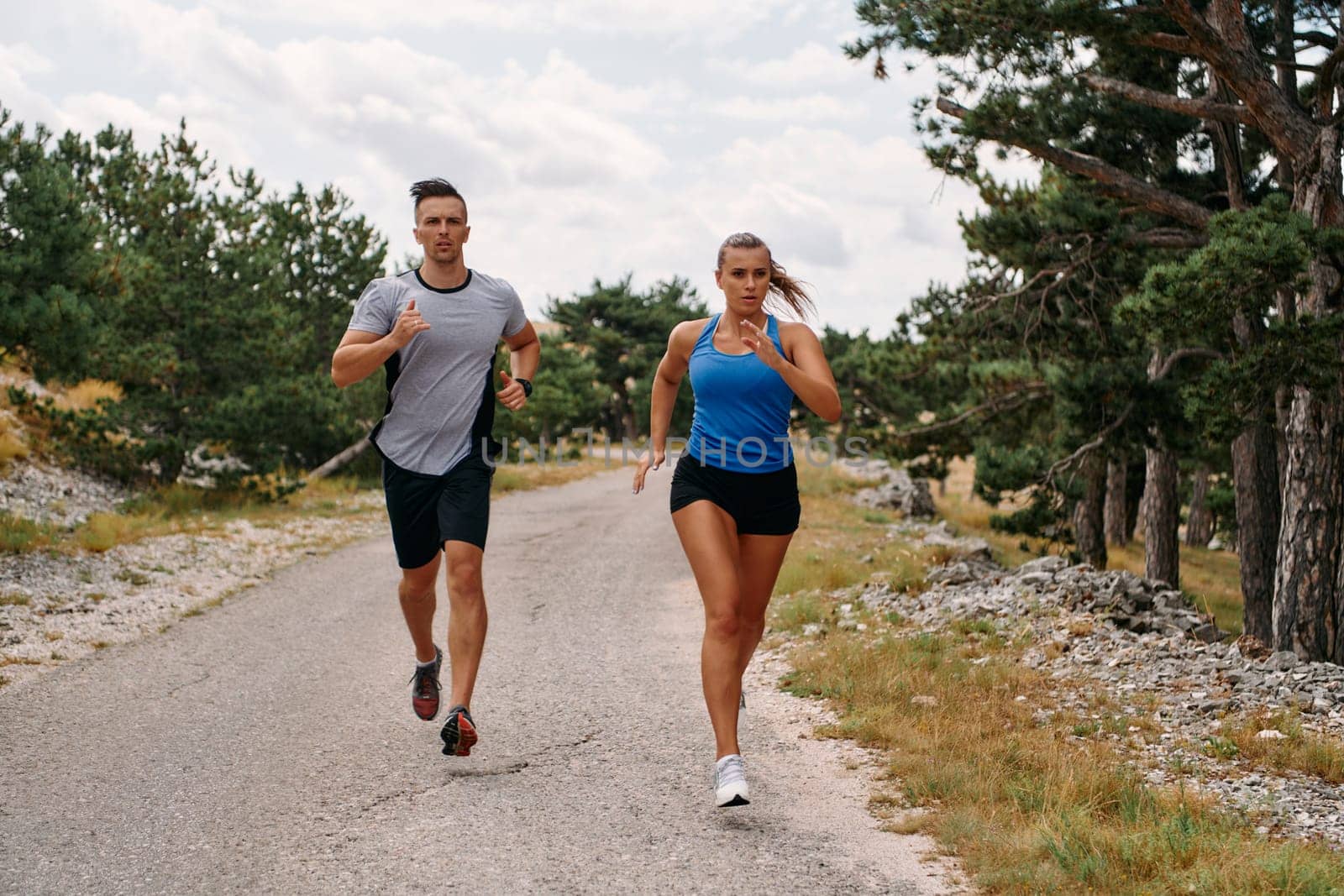 A couple dressed in sportswear runs along a scenic road during an early morning workout, enjoying the fresh air and maintaining a healthy lifestyle.