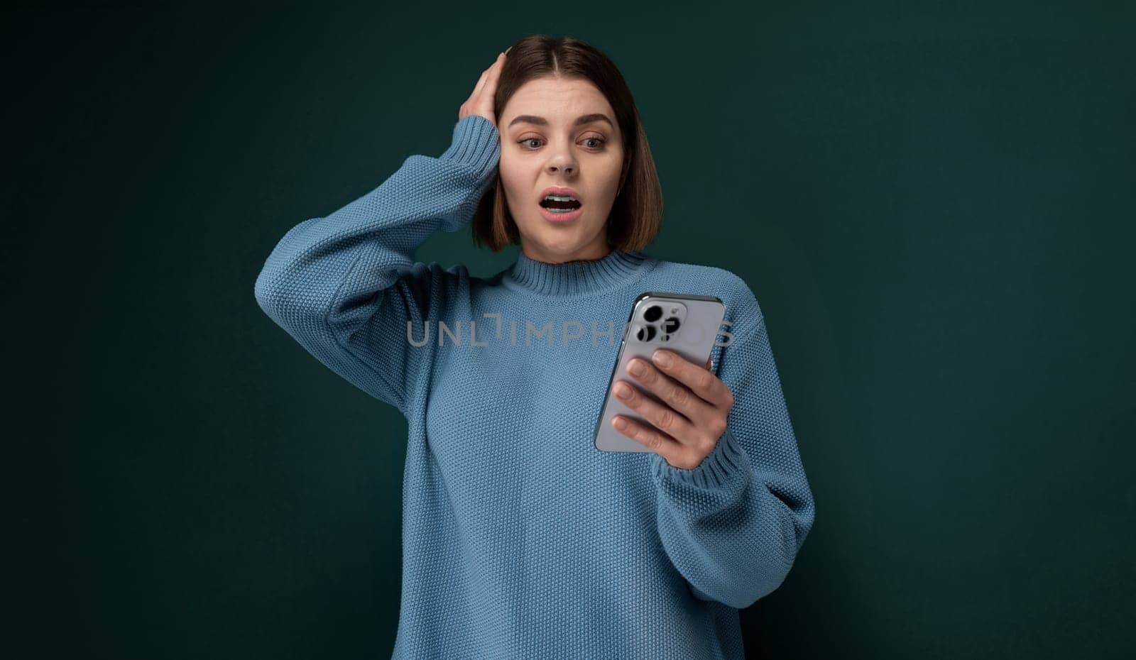 A woman wearing a blue sweater is holding a cell phone in her hand. She appears to be focused on the screen, possibly texting or browsing.