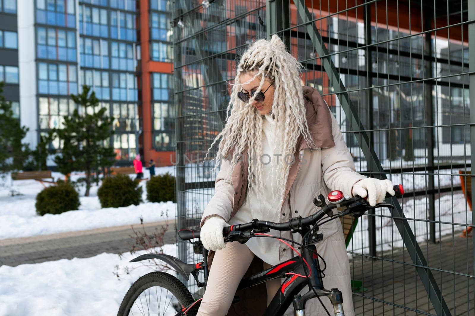 A woman with long white hair is riding a bike in the snow. She is bundled up in warm clothing as she pedals through the cold, snowy landscape.