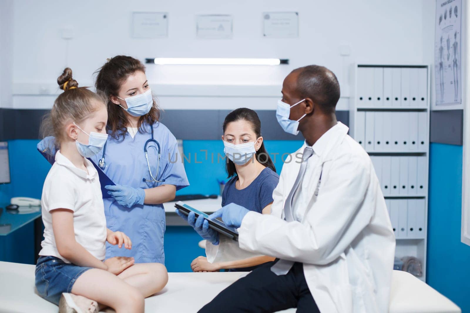 Doctor and nurse conducting a checkup, providing advice to a girl and her mother in a medical office. Healthcare professionals have a consultation with patients. Face masks worn for protection.