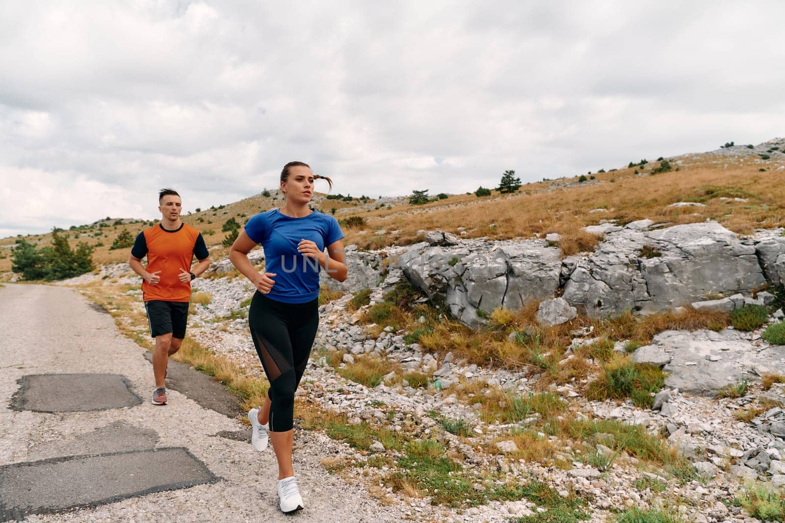 A couple dressed in sportswear runs along a scenic road during an early morning workout, enjoying the fresh air and maintaining a healthy lifestyle.