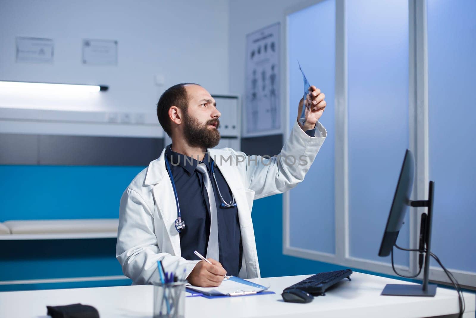 Young doctor examining a CT scan of patient and taking notes on his notepad. Caucasian male healthcare professional inspecting a chest X-ray image of an individual.