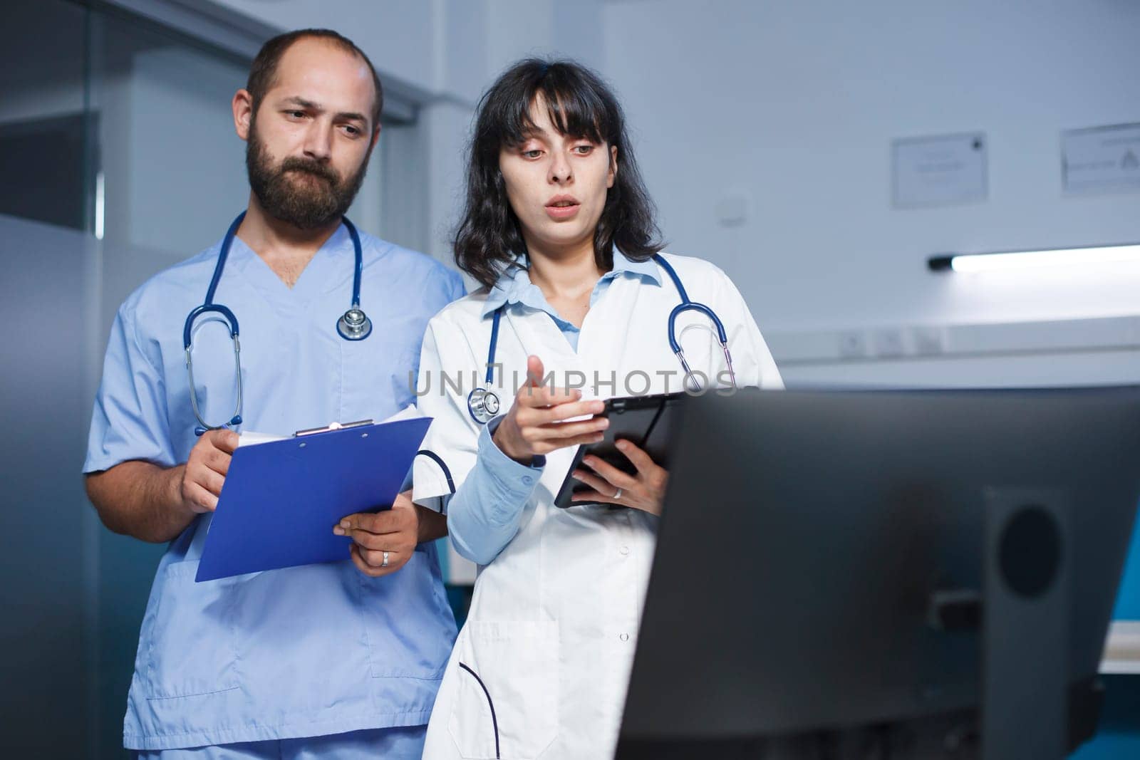 Caucasian man with a clipboard talking about patient appointments with a woman holding a digital tablet in the clinic. Female doctor discussing healthcare and medication with a male nurse.