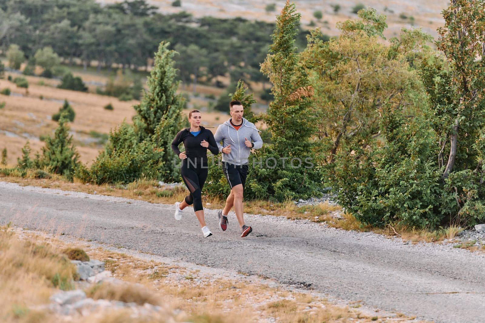 A couple dressed in sportswear runs along a scenic road during an early morning workout, enjoying the fresh air and maintaining a healthy lifestyle by dotshock