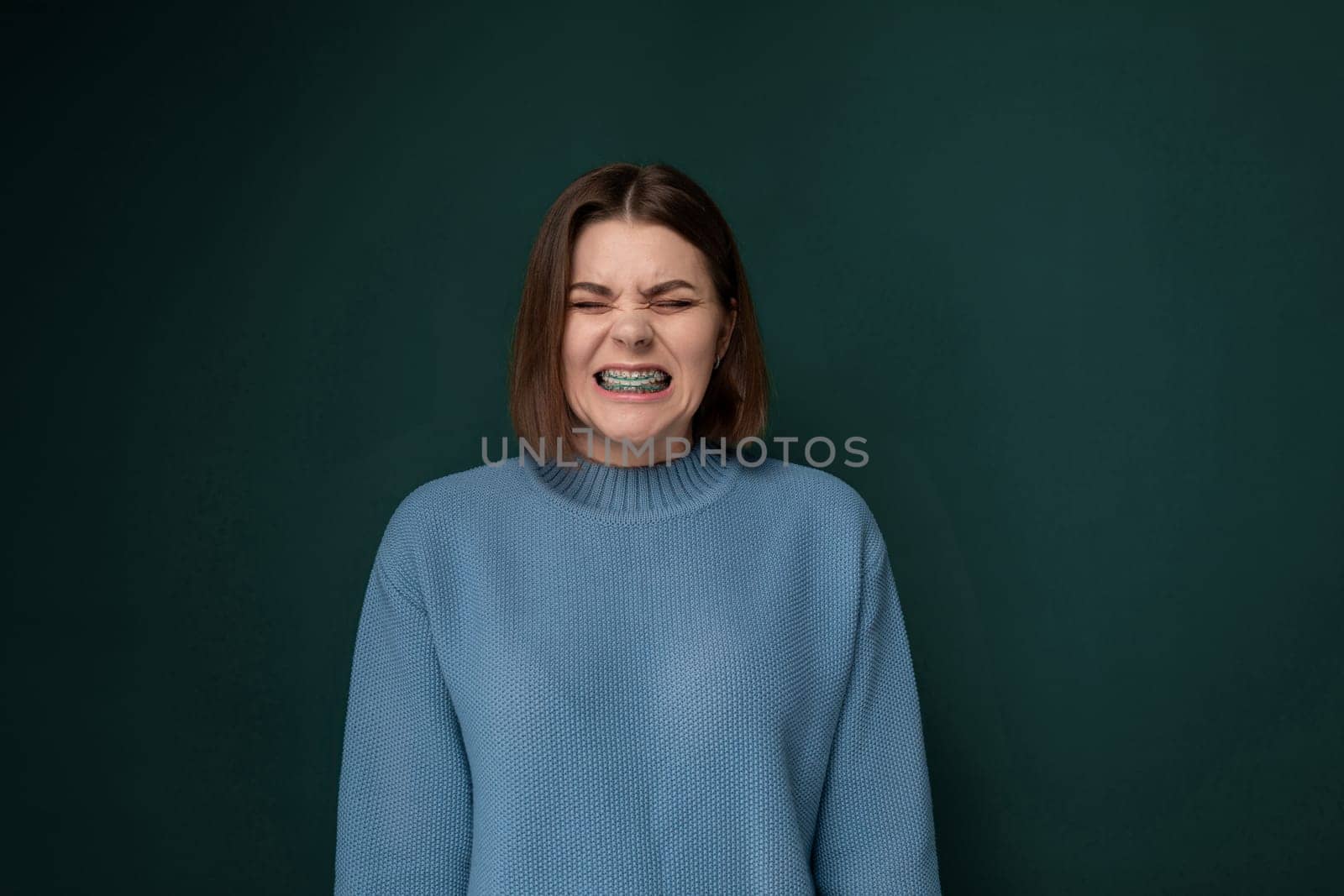 A woman wearing a blue sweater is contorting her facial expression, displaying emotions or reactions. The background is simple and focuses on the subjects actions.