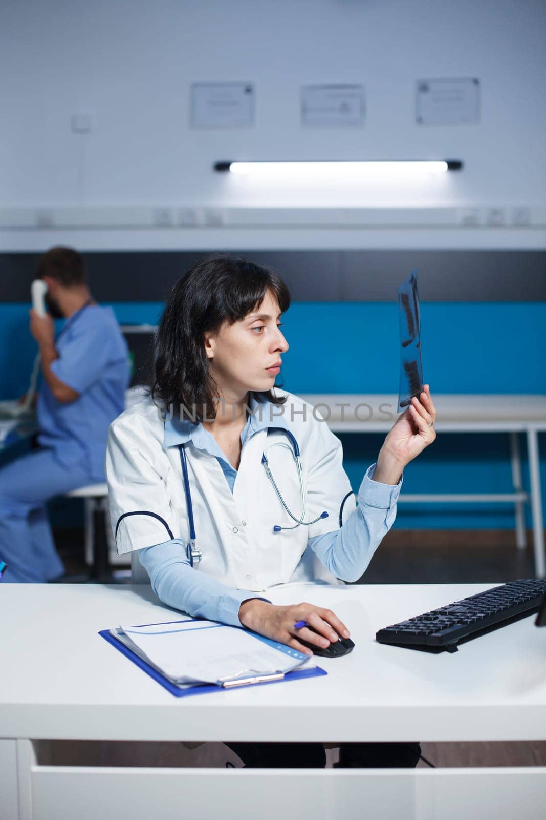 Physician holding a radiography analyzing lungs expertise, typing a medical report on computer, and arranging health care therapy to help cure a patient. Medic working overtime in the hospital office