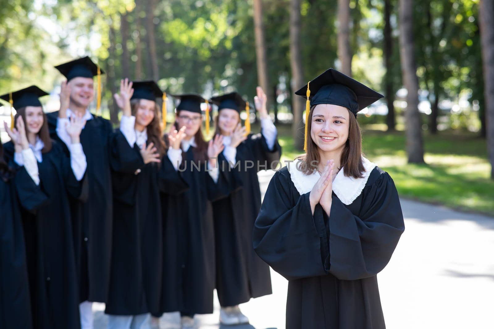 Group of happy students in graduation gowns outdoors. A young girl in the foreground
