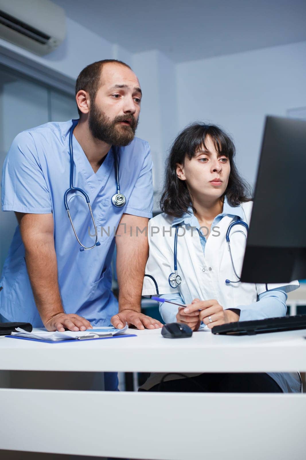 Healthcare professionals collaborate in a hospital, discussing patient care, utilizing digital devices like desktop computers. Effective communication and teamwork are highlighted.