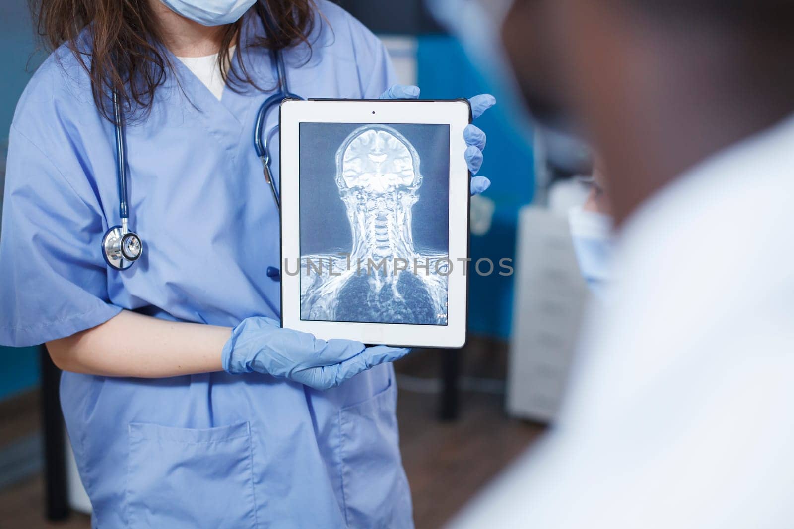 In medical office, doctor uses tablet to analyze a scan of a patient's skull. Selective focus of nurse in blue scrubs holding a device with an x-ray image. Advanced technology and expert care.