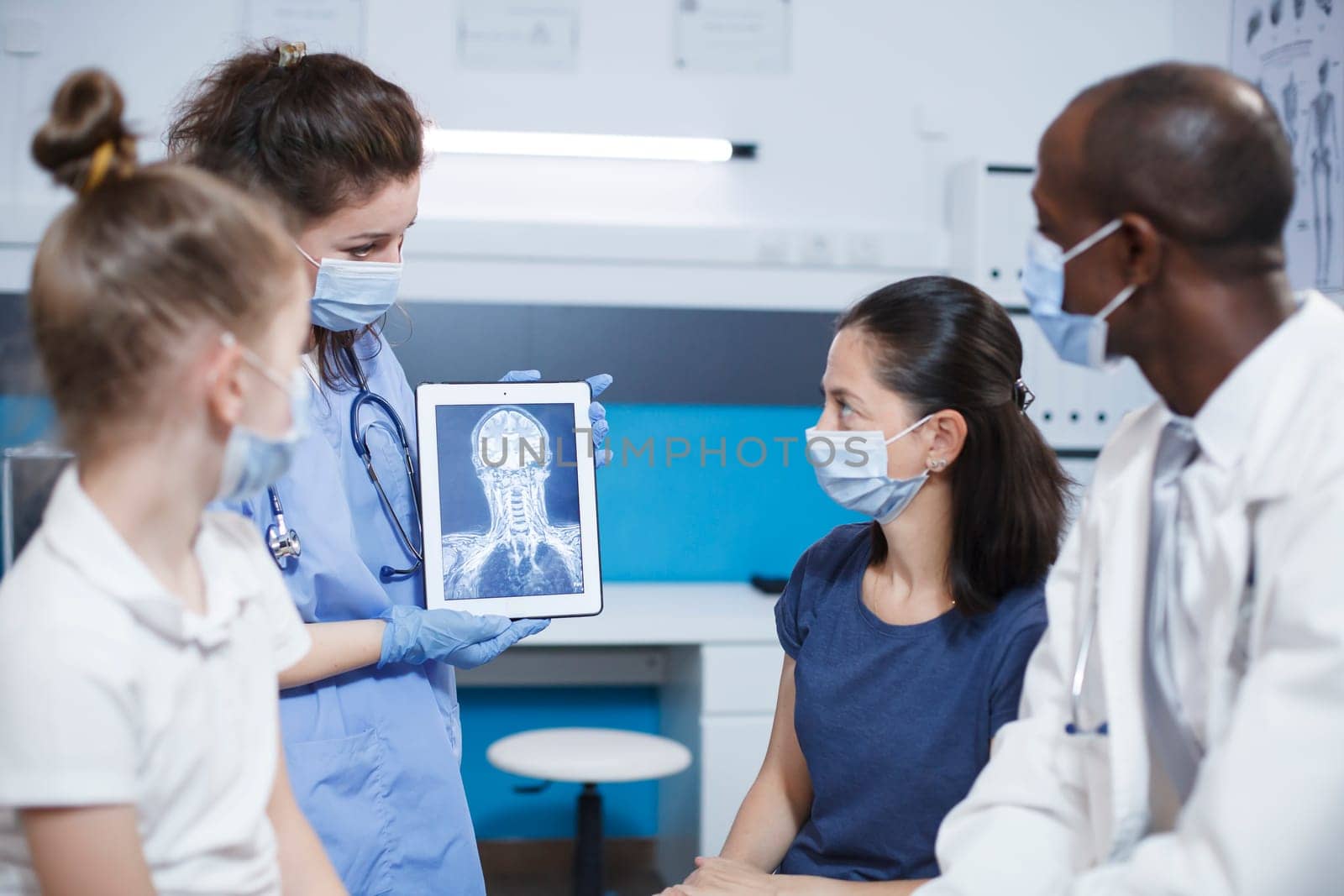 Doctor analyzes a brain scan while explaining the results, in a modern clinic with state of the art technology. Nurse holding a tablet displaying an x ray image of a head of a patient.