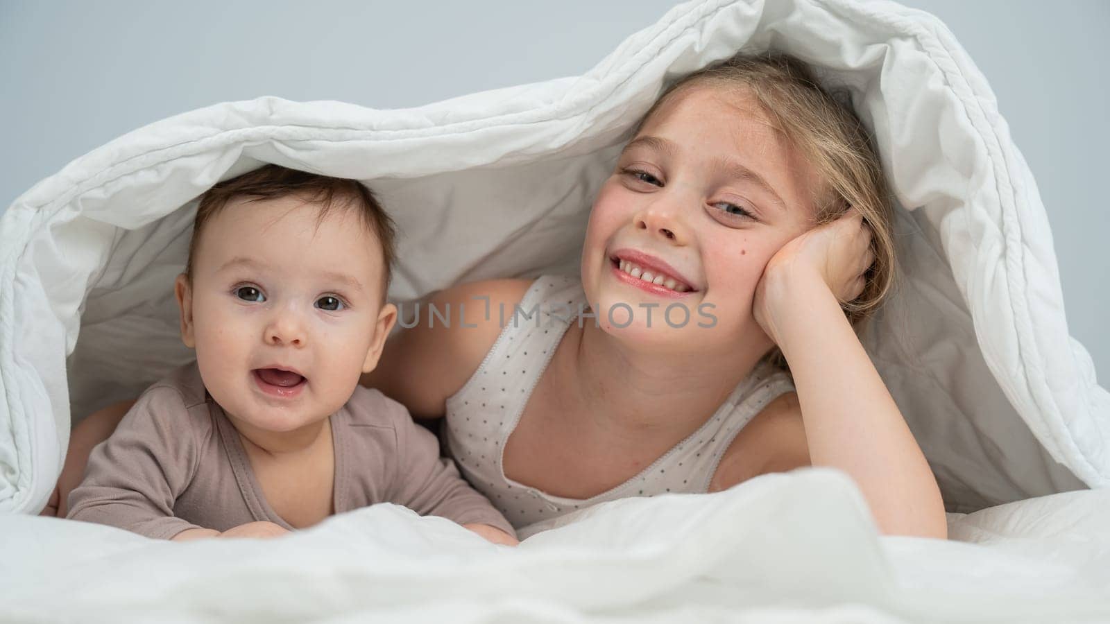 Little girl and her newborn brother hiding under the blanket