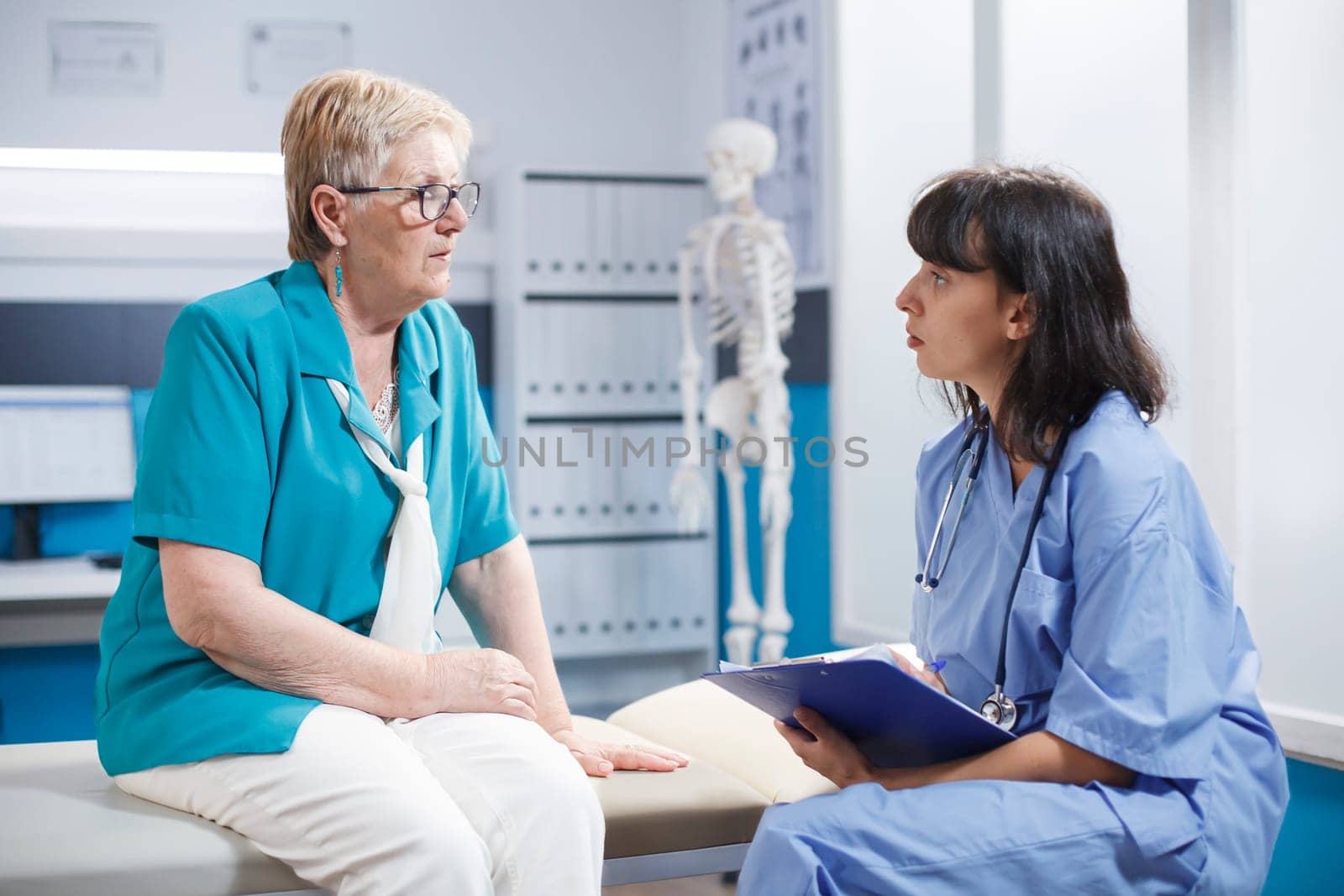 Female practitioner consulting aged woman with physical injury in office. Medical assistant doing checkup on old patient for orthopedic diagnosis and recovery, talking about pain relief.