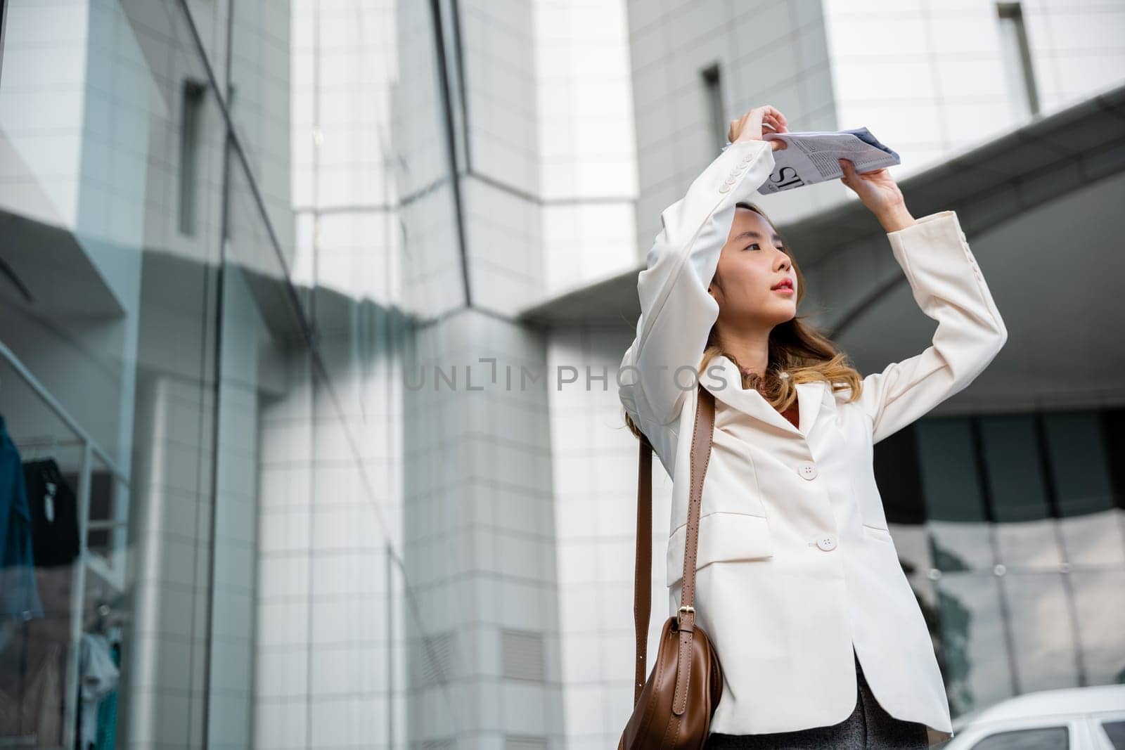 Portrait of Business woman walking out the building after finish work shade sun UV with newspaper. Young Asian woman wearing white shirt while cover the sun by news paper on the streets of downtown