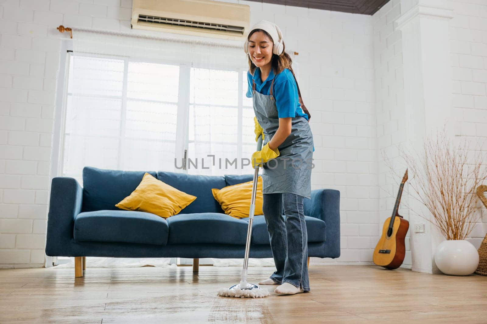 Asian teen happy cleanup, maid listens dances with headphones. Joyful occupation paired with music excitement. Modern housework tech vibe. Happy and Fun During Cleaning