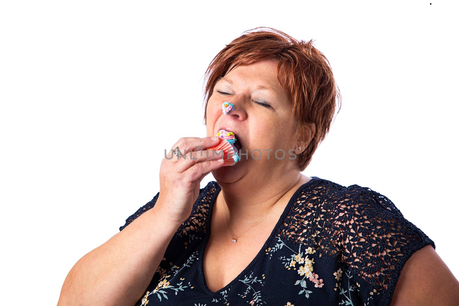 Overweight fifty something woman stuffing a cupcake in her mouth