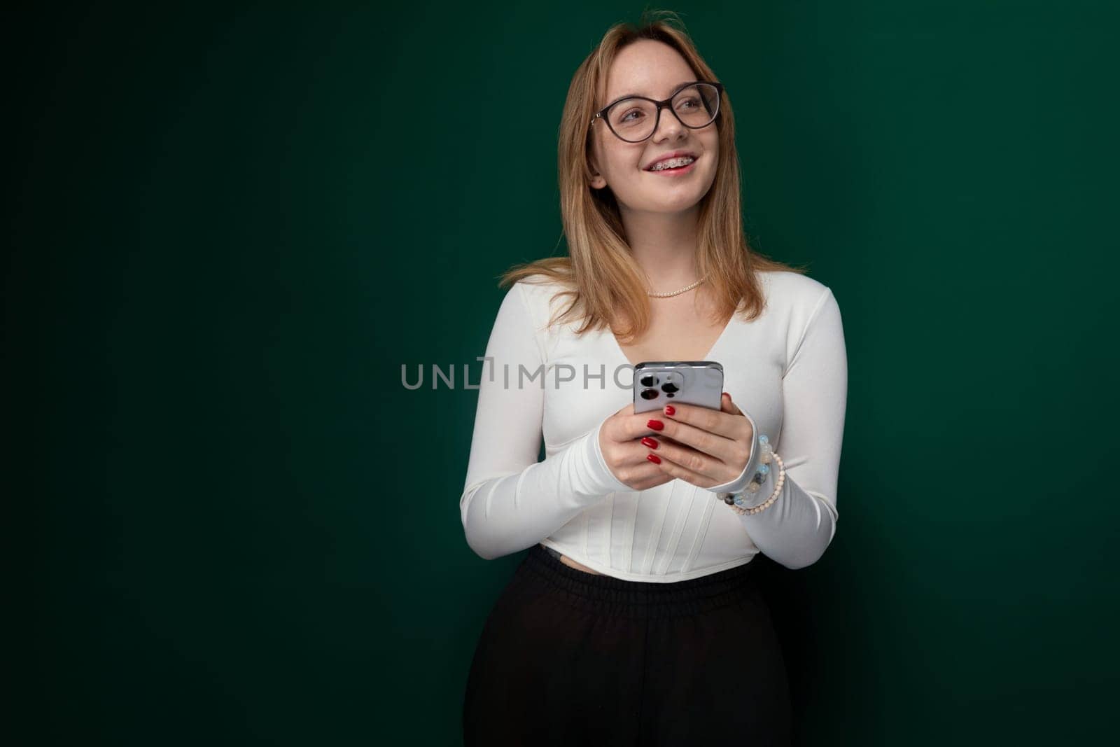 A woman with glasses is seen holding a cell phone in her hand, with her eyes focused on the screen. She appears engaged in the content on the device, possibly texting or browsing. The womans expression is intent, and her body language suggests concentration.