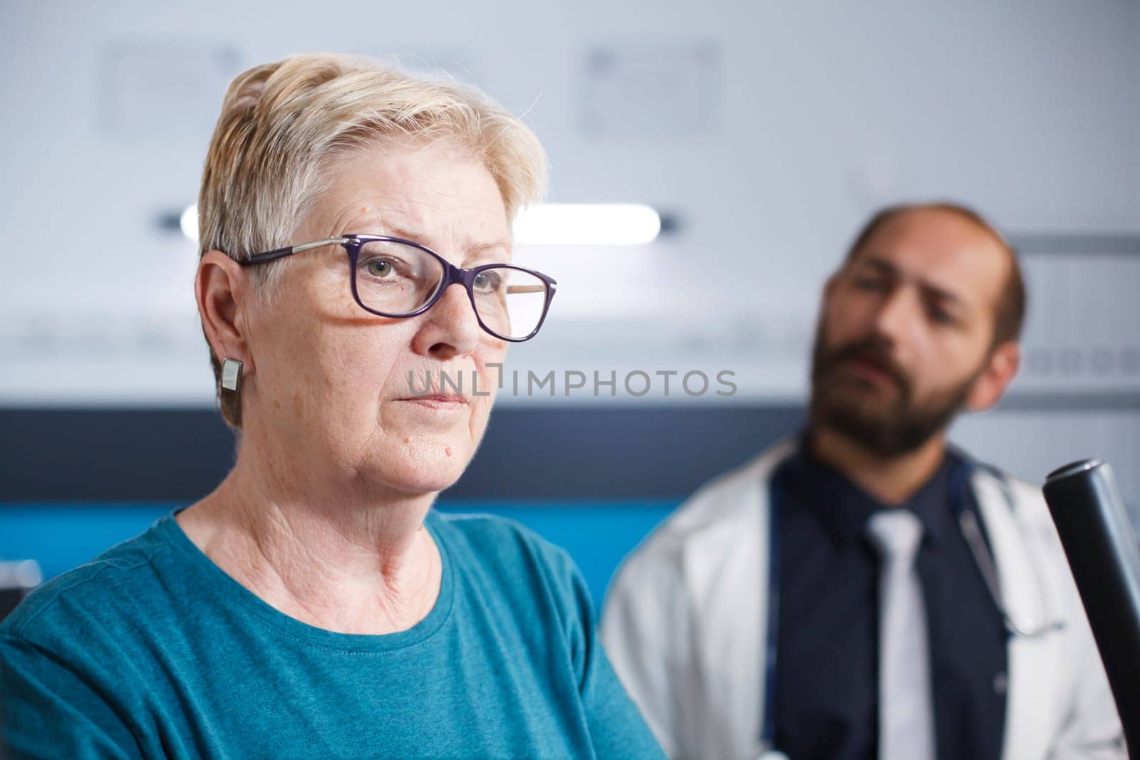 Close-up of an elderly patient training with sports equipment and rehabilitation gear. Portrait of old woman with glasses undergoing physiotherapy with professional male doctor.