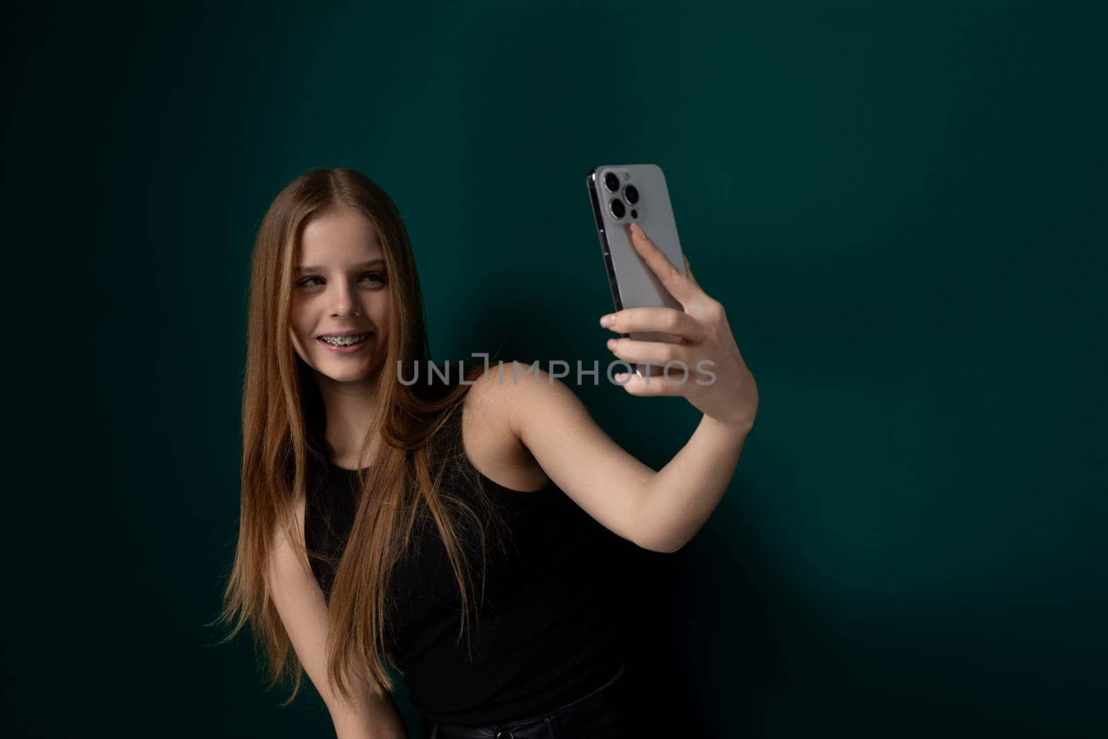 A woman is seen holding a cell phone at arms length, smiling and posing for a selfie. She is capturing the moment on her device to share with others on social media.