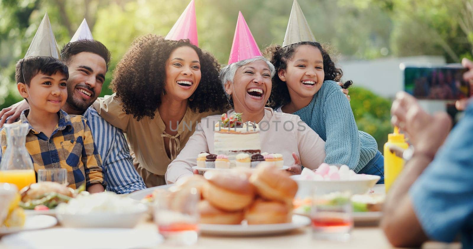 Family, birthday party and people with phone for photo in garden with cake, happy and love. Grandmother, parents and children with smartphone for memory, dessert and home in backyard on social media by YuriArcurs