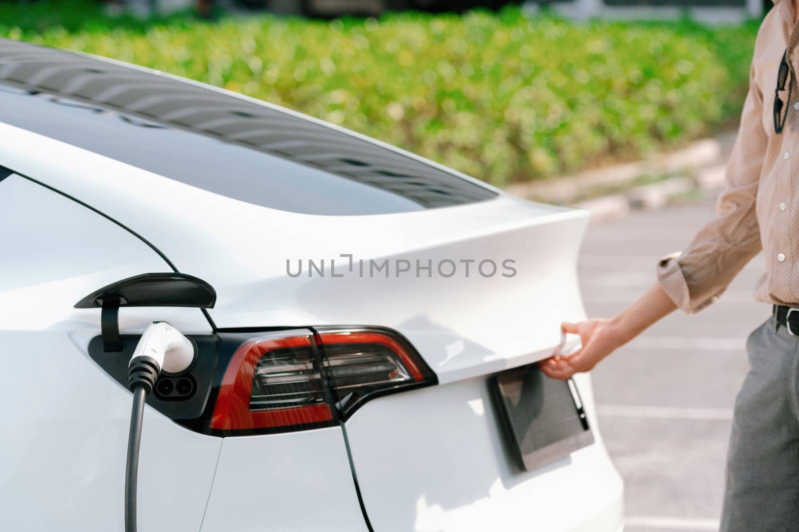 Young woman open trunk while EV car recharging battery. Expedient by biancoblue