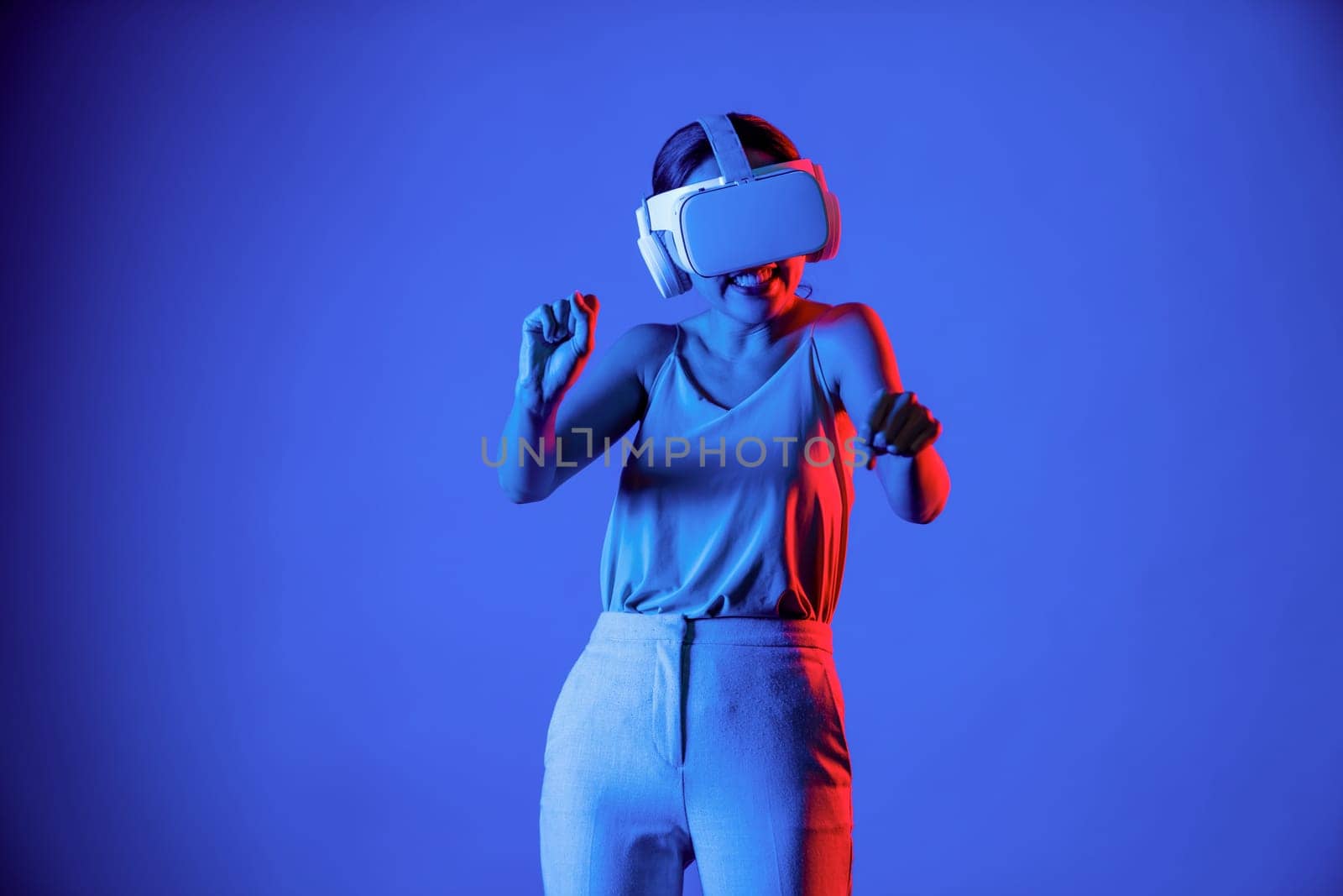 Smart female stand surrounded by neon light wearing VR headset connecting metaverse, future cyberspace community technology. Elegant woman enjoy playing car racing games in meta world. Hallucination.