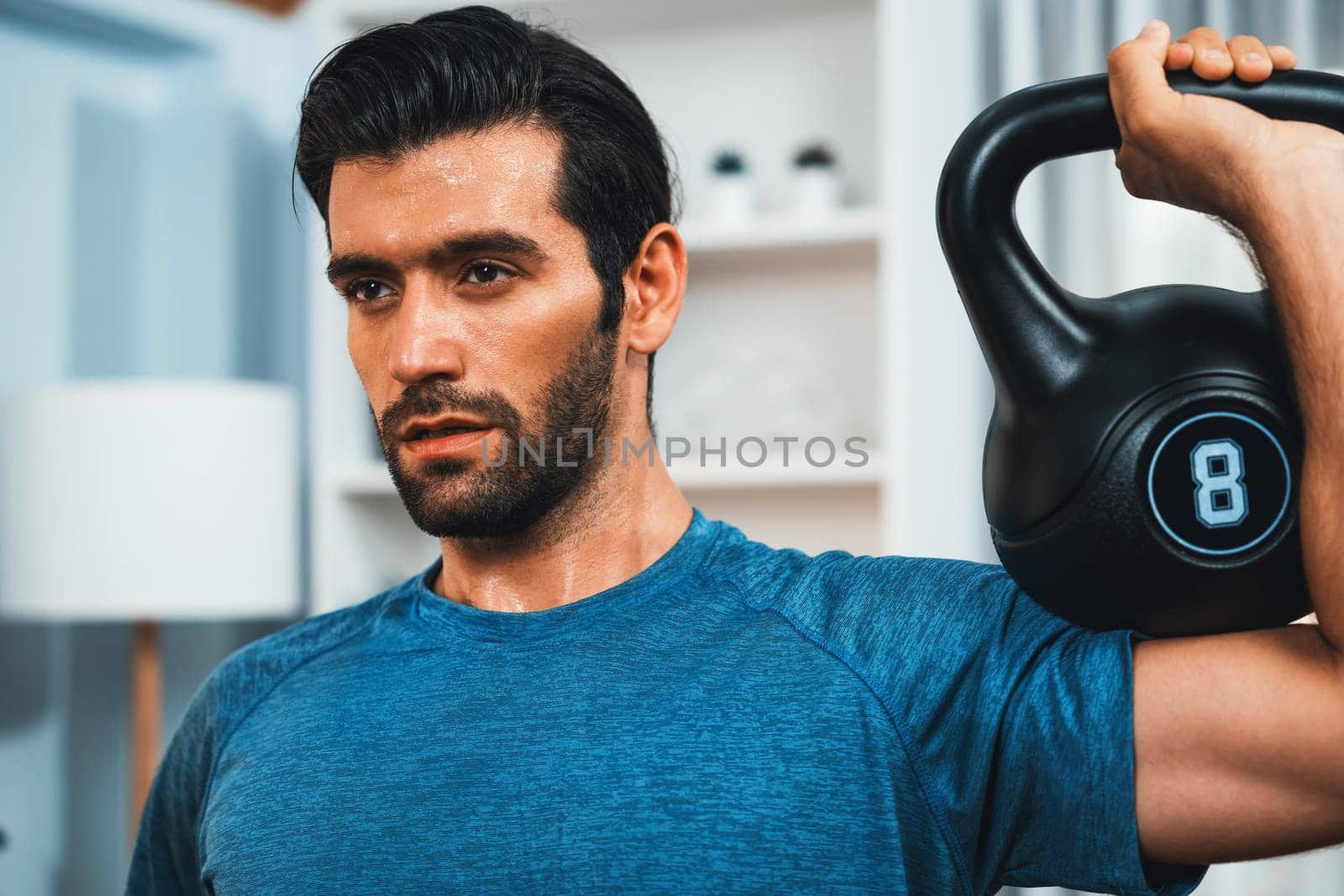 Athletic body and active sporty man lifting kettlebell weight for effective targeting muscle gain at gaiety home as concept of healthy fit body home workout lifestyle.