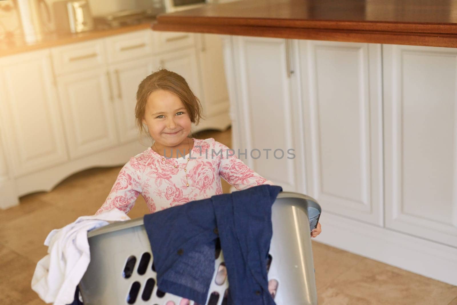 Smile, basket and child with laundry in home for learning to clean with development and growth. Happy, kitchen and portrait of girl kid with clothes for washing with housekeeping at apartment. by YuriArcurs