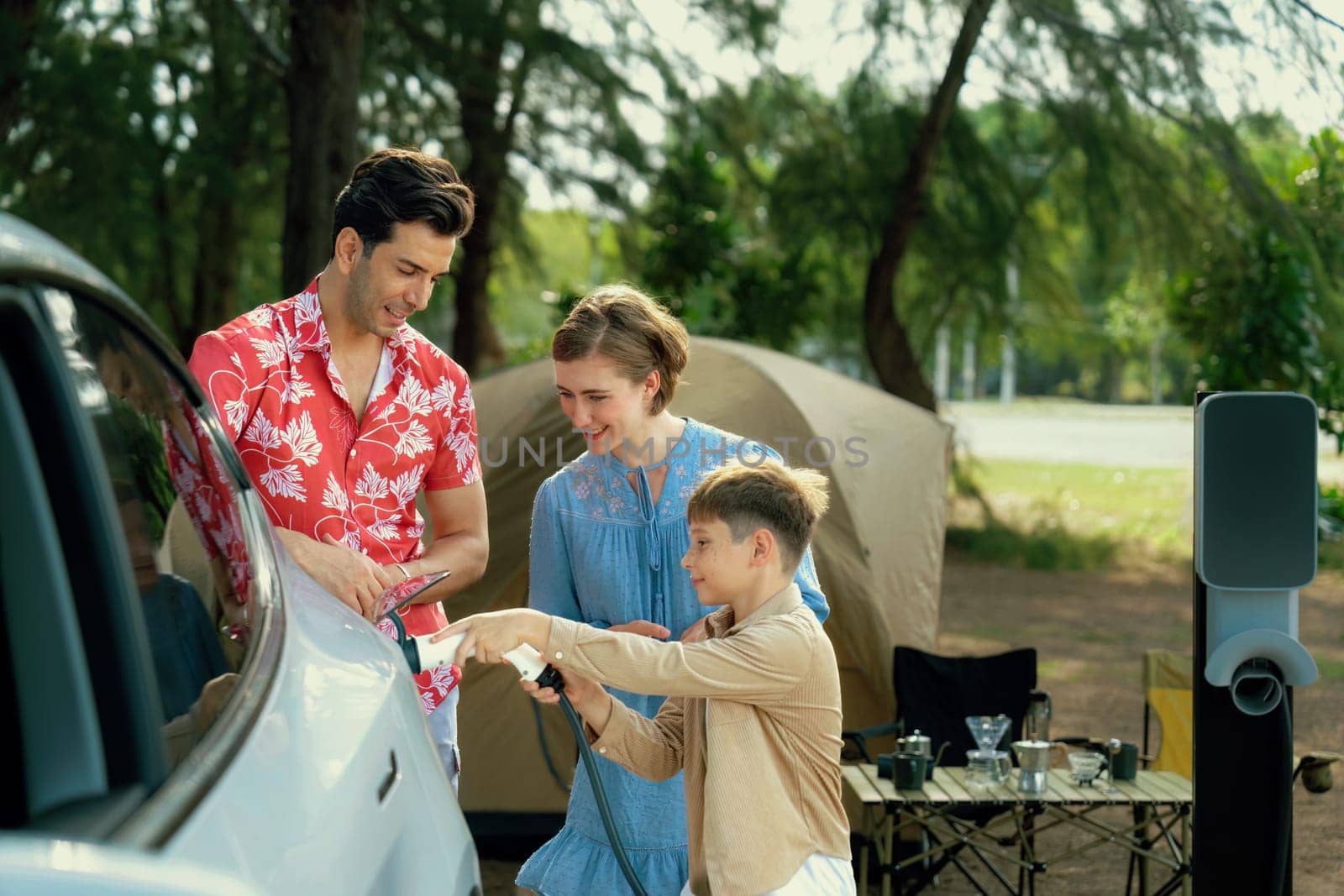 Lovely family recharge EV car with EV charging station in campsite. Perpetual by biancoblue