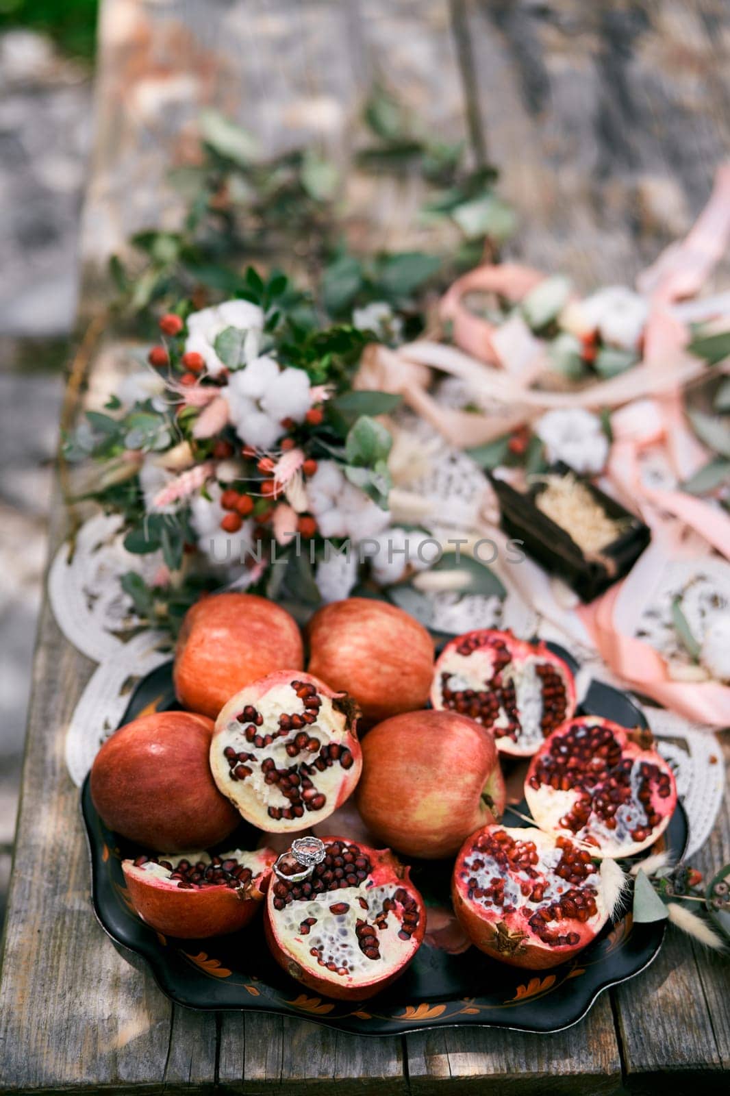 Wedding rings lie on half a pomegranate on a plate of fruit on the table next to the wedding bouquet. High quality photo