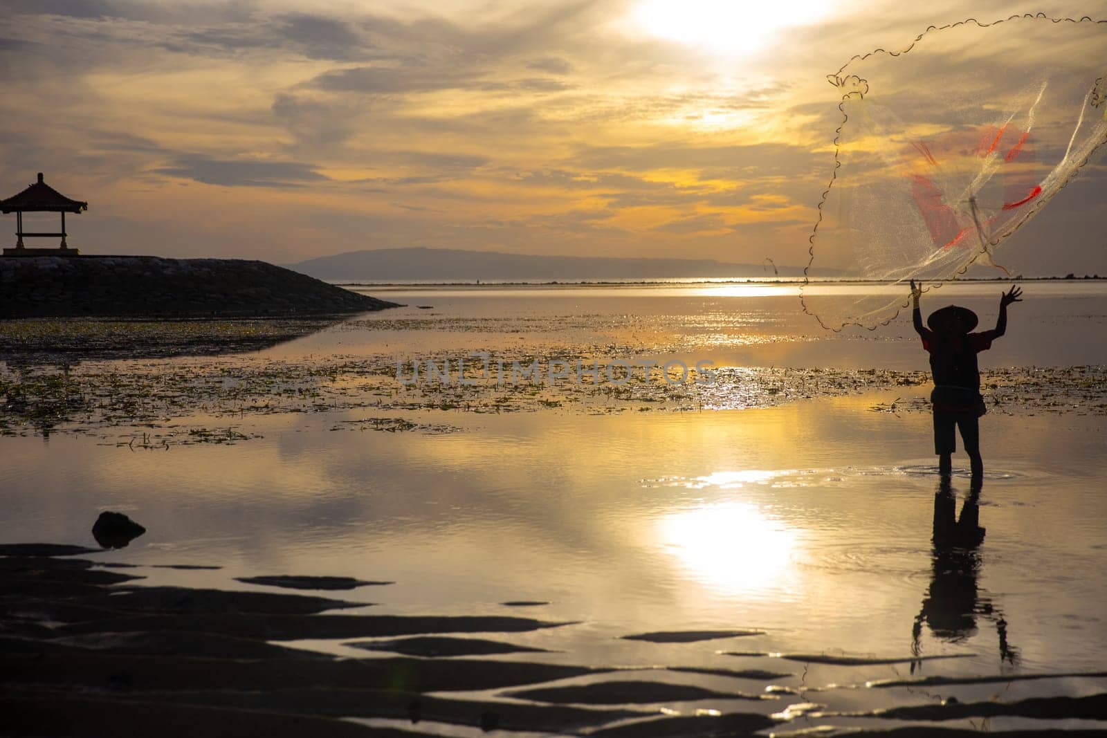 Indonesian Fisherman throwing a net with a pagoda in the background