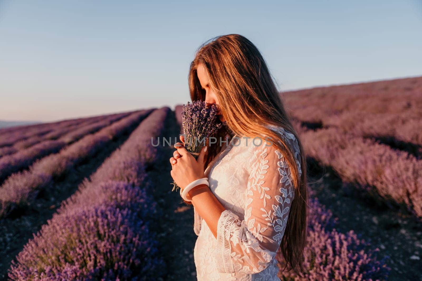 Woman lavender field. Happy carefree woman in a white dress walking in a lavender field and smelling a lavender bouquet on sunset. Ideal for warm and inspirational concepts in wanderlust and travel. by panophotograph