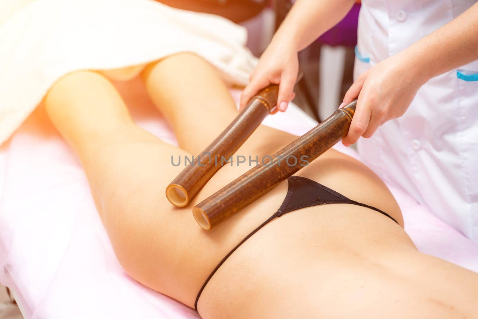 Woman having massage with bamboo stick in wellness center. by Matiunina