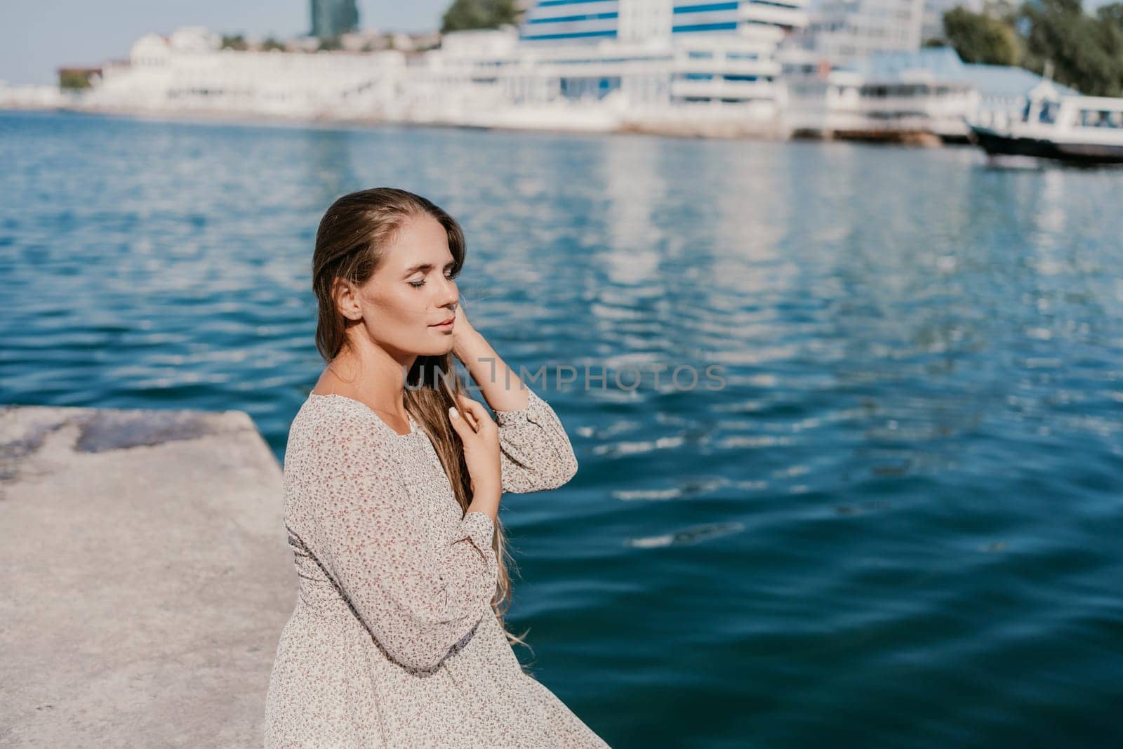 A woman is sitting in the water wearing a white dress. The water is calm and blue. The woman is enjoying the moment and taking in the beauty of the scene. by Matiunina