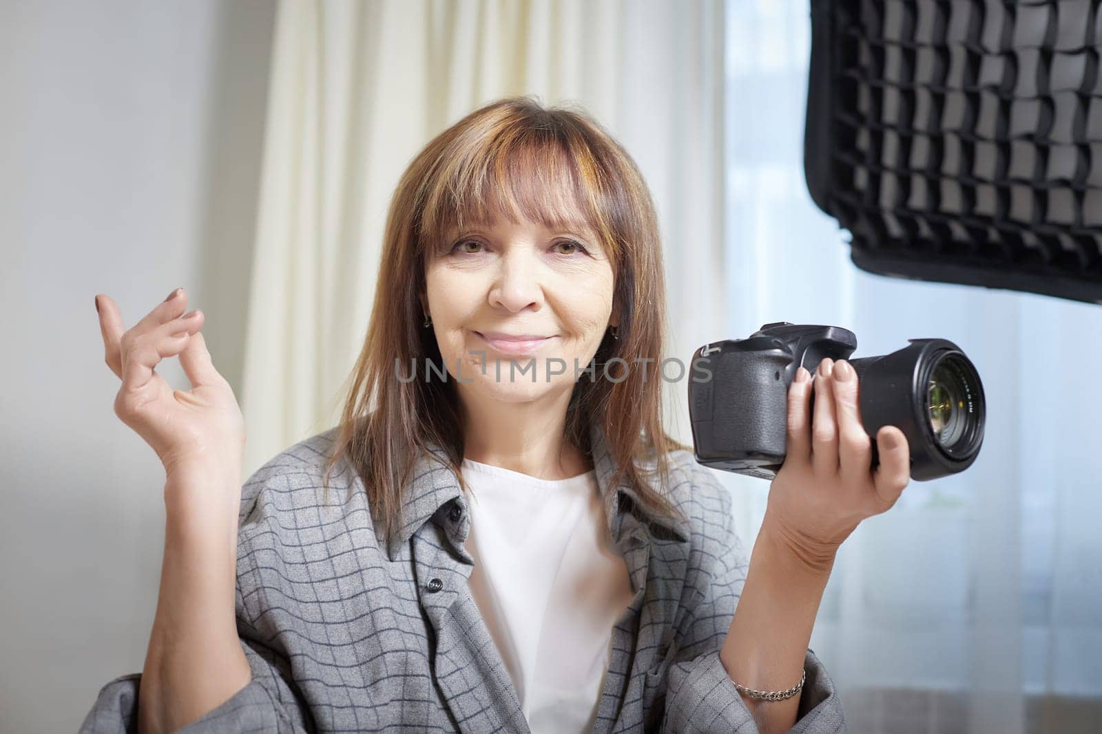 Senior old elderly woman with black camera with a large lens indoors in the studio. Professional photographer. Age Hobby