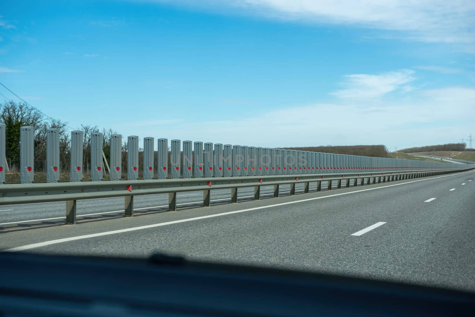 A road with a long line of metal posts with red hearts on them. The road is empty and the sky is clear