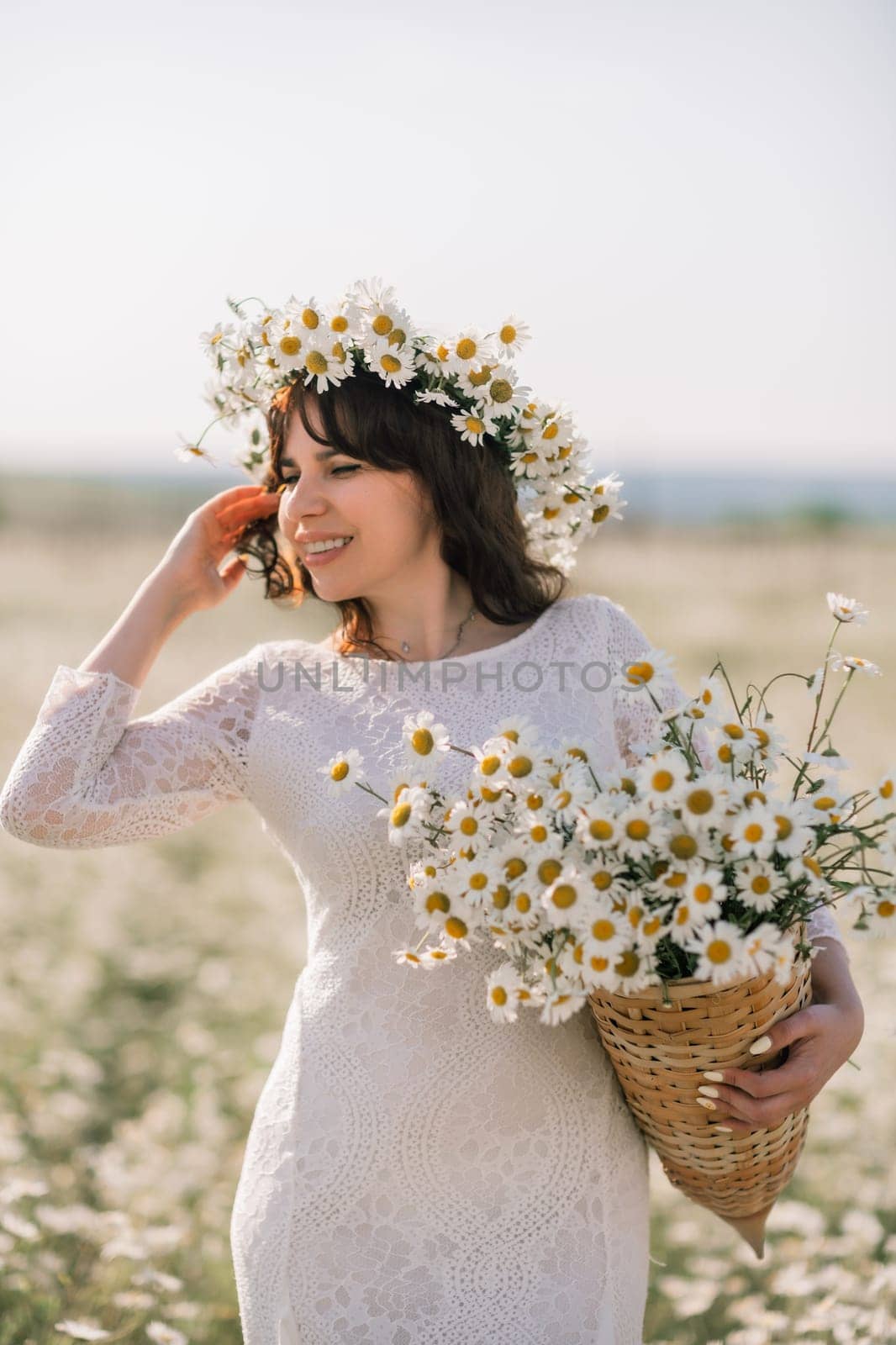 Happy woman in a field of daisies with a wreath of wildflowers on her head. woman in a white dress in a field of white flowers. Charming woman with a bouquet of daisies, tender summer photo by Matiunina