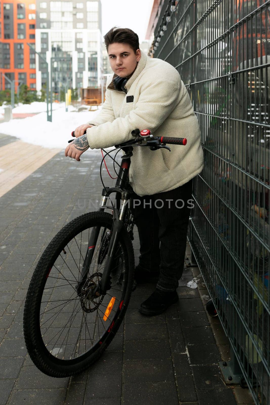 A young European man with a winter jacket walks around the city with a bicycle.