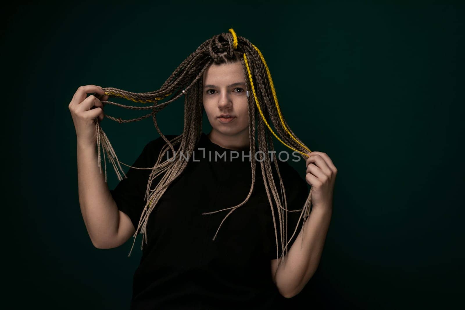 A woman with dreadlocks on her head is standing and looking at the camera. She has long, twisted hair that falls down her back. The dreadlocks are neatly styled and showcase her unique hair texture.