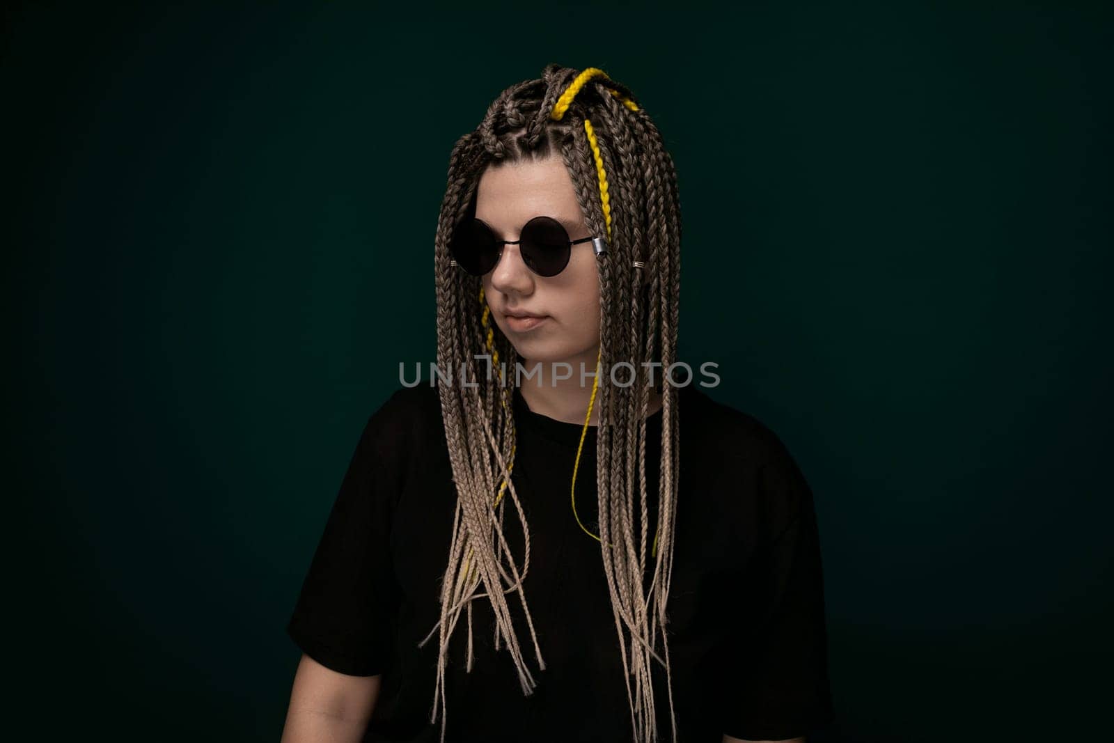 A woman with dreadlocks is seen wearing a black shirt, looking directly at the camera in a neutral pose. Her dreadlocks are styled neatly and fall down her shoulders. She appears confident and poised.