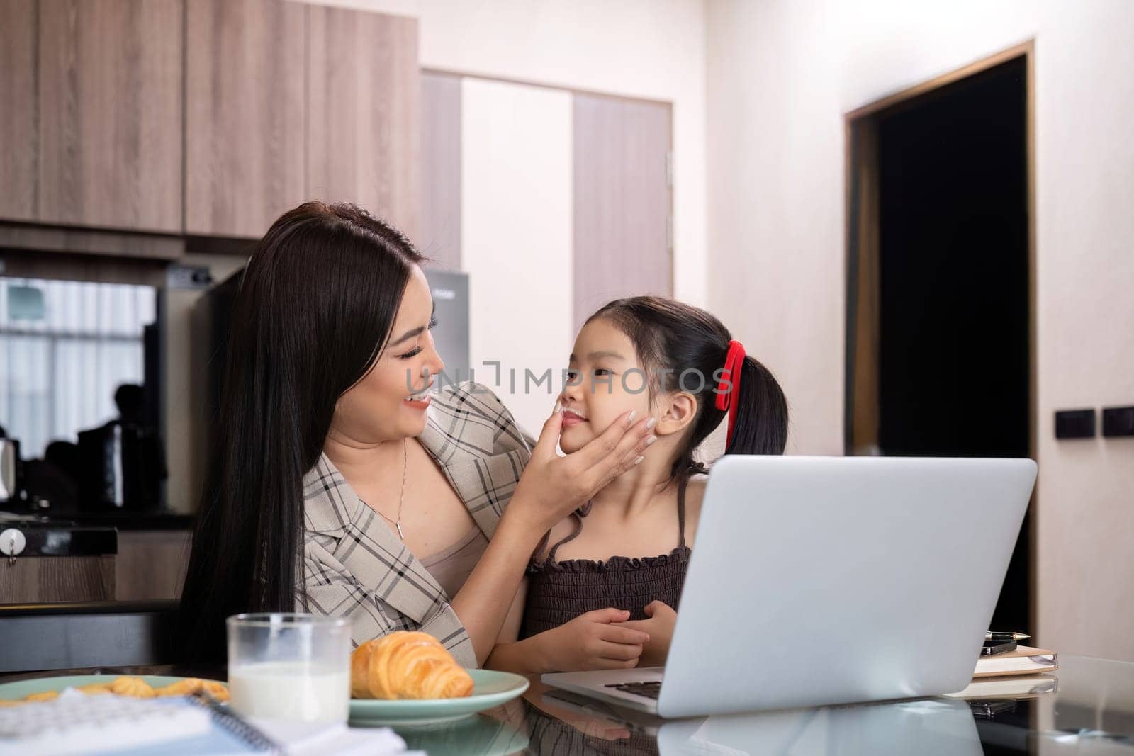A young single mother receives a snack and eats it with her daughter while she works at home on her laptop. by wichayada