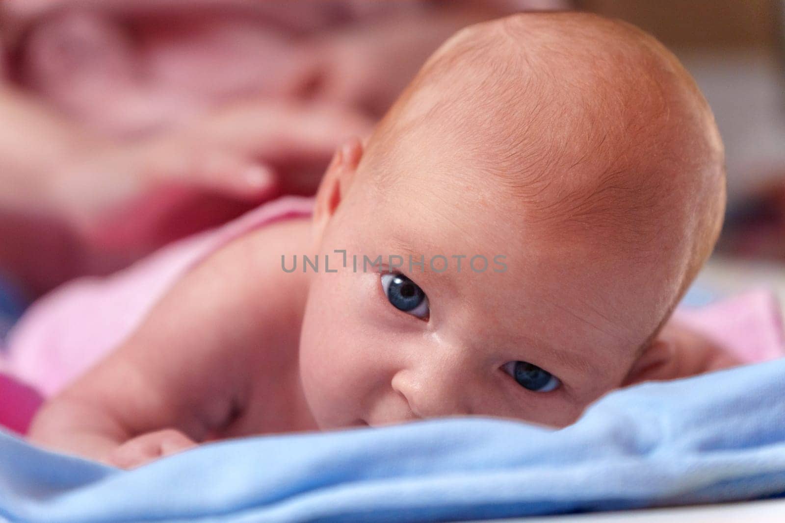 Newborn baby, at the tender age of two months, lies comfortably while curiously looking at the world around with bright, expressive eyes.