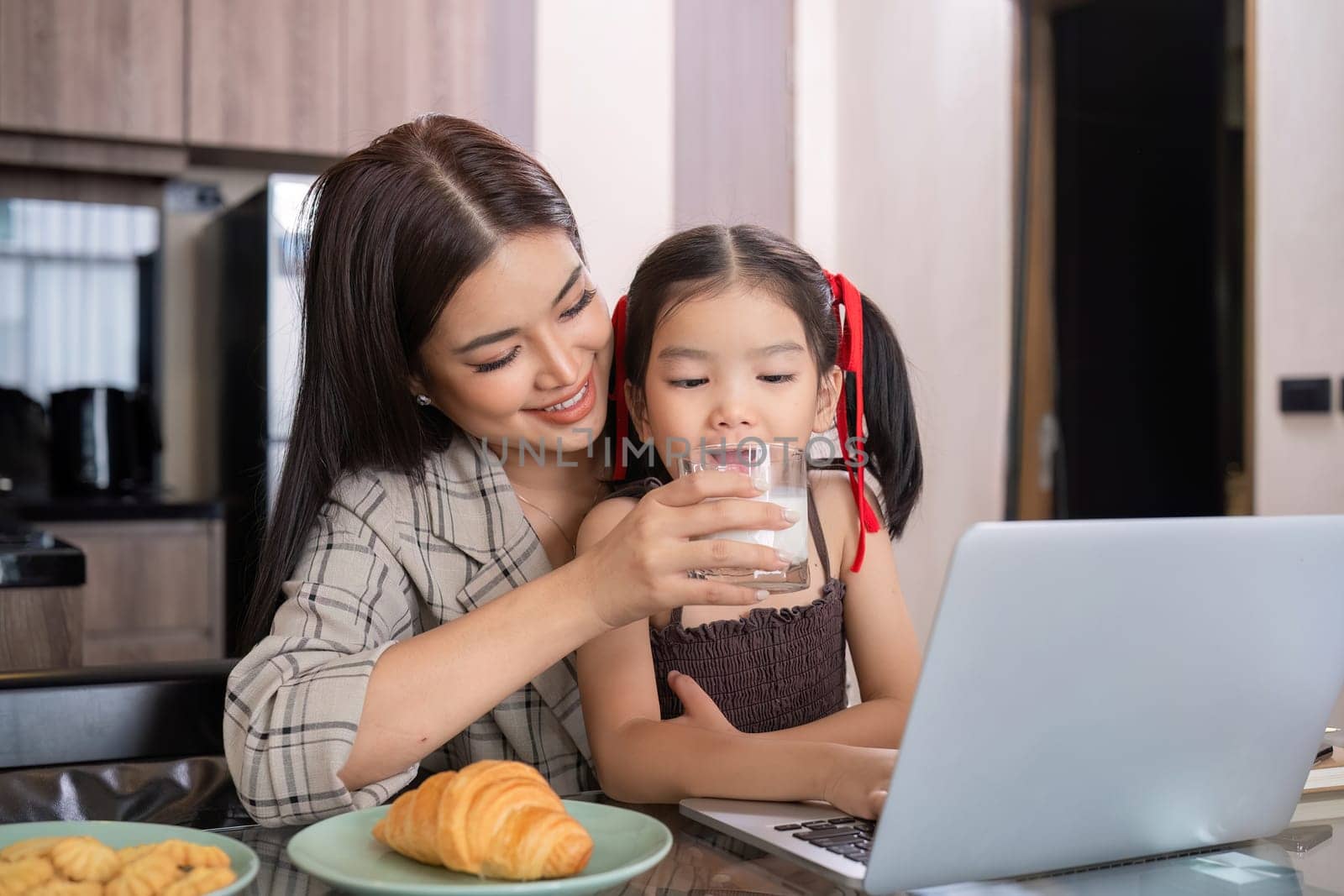 A young single mother receives a snack and eats it with her daughter while she works at home on her laptop..