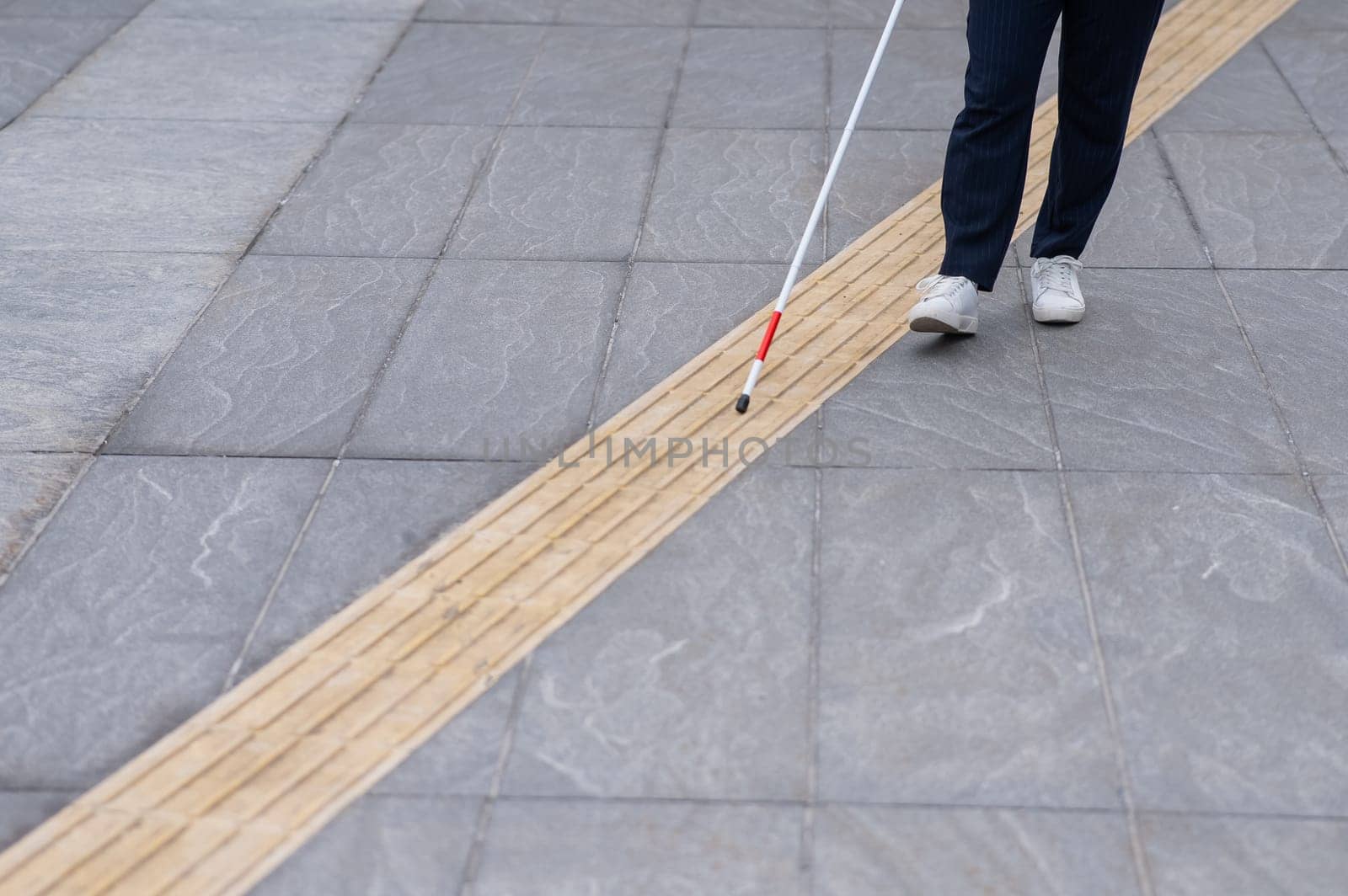 Close-up of the legs of a blind businesswoman walking along a tactile tile with a cane