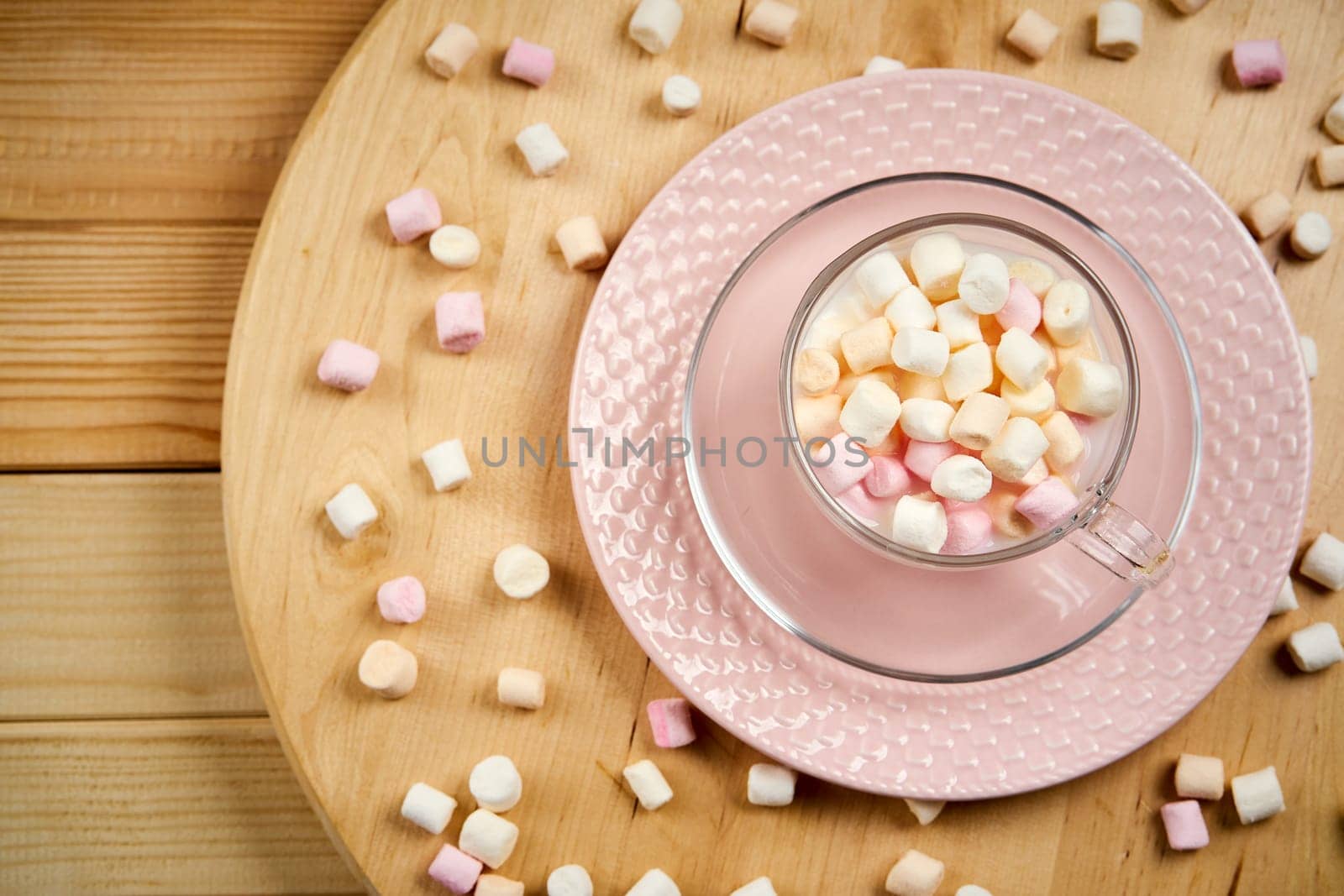 Cup with hot milk and colorful marshmallows on bright wooden table