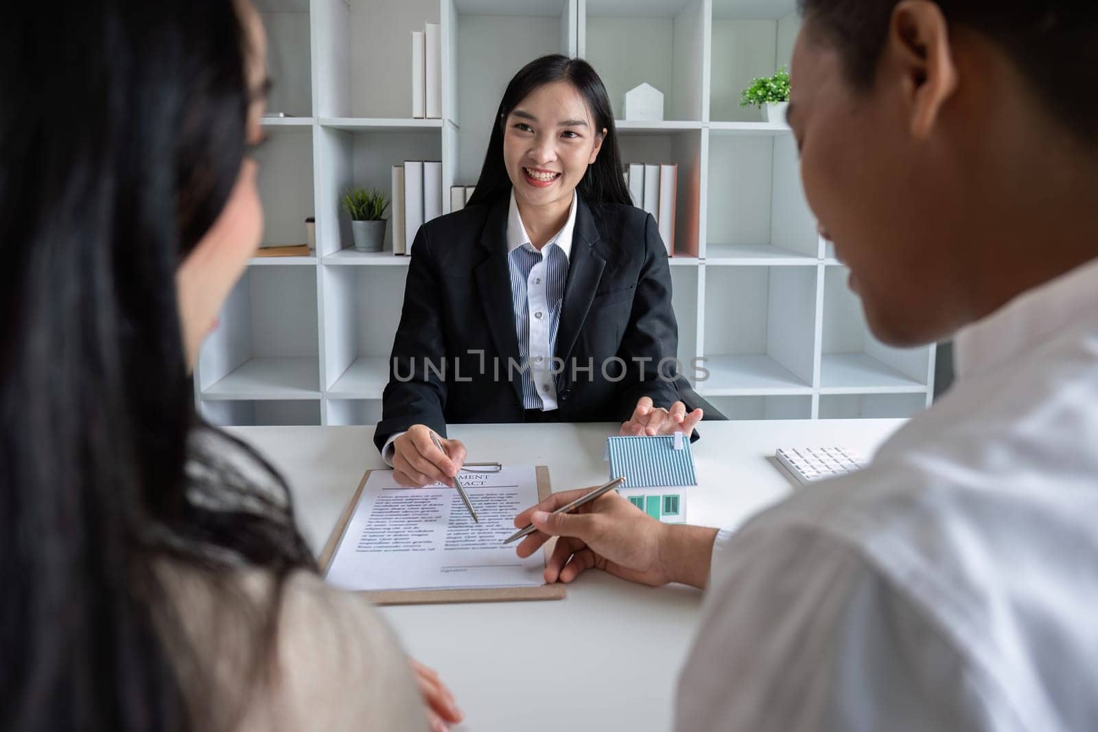 A real estate agent or insurance agent presents a house plan and insurance contract to an Asian couple..