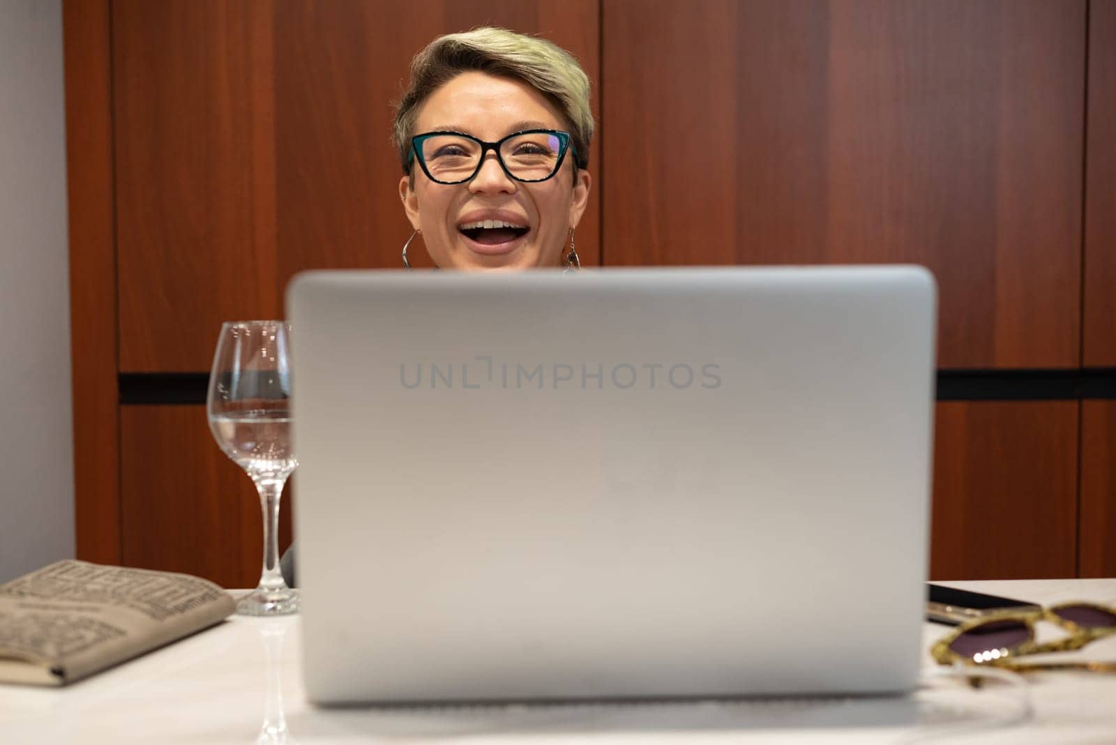 girl with short hair and glasses indoors at a laptop laughs and smiles emotionally and cheerfully while working and chatting
