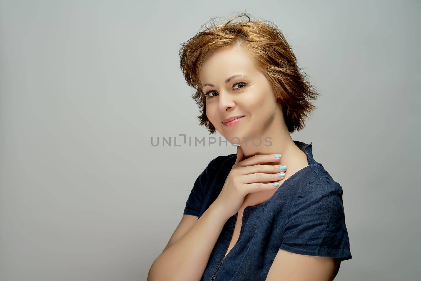 Portrait of young attractive red-haired woman in navy blue dress on gray background
