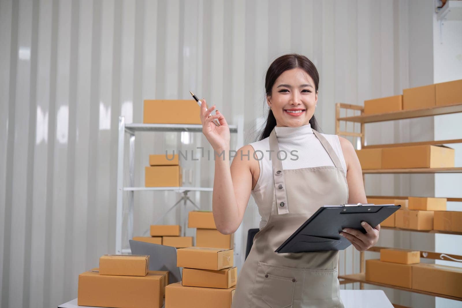 A small SME business owner writes inventory and shipping information on a clipboard in his home office. Small business operators preparing to ship to customers.