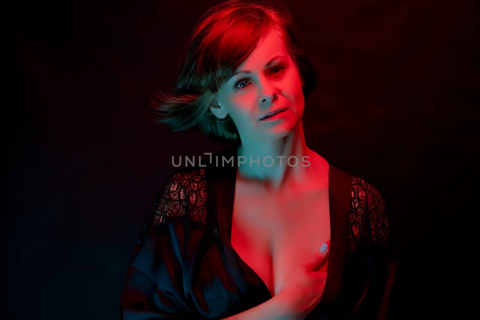 Beautiful attractive young woman posing in satin bathrobe in neon light in the studio.